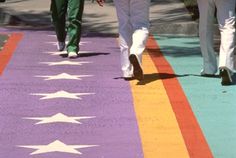 two people walking down the sidewalk painted with white stars and rainbow colors, while another person in green pants walks behind them