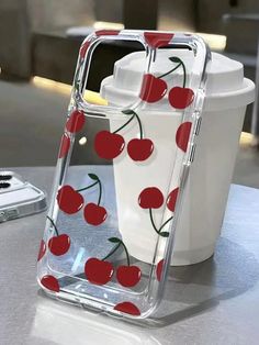 a phone case with cherries on it sitting next to a cup