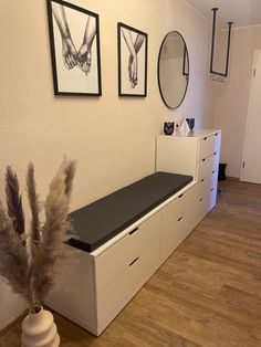 an empty room with white drawers and pictures on the wall above it, along with a plant in a vase