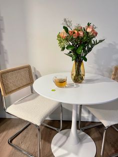 a white table with two chairs and a vase filled with flowers on top of it