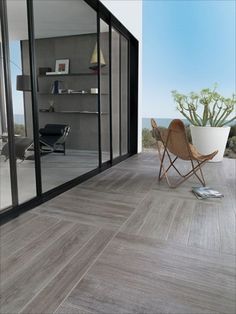 a chair sitting on top of a wooden floor next to a glass wall with a potted plant