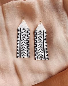 two black and white earrings sitting on top of a pink blanket