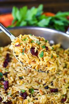 a spoon full of rice with cranberries and parsley on top is being lifted from a pan