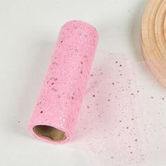 a roll of pink glittered paper next to a wooden object on a white surface