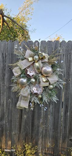 a wreath on a fence decorated with bells and greenery in front of a wooden fence