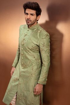 a man in a green sherwa with gold thread work on the jacket and pants