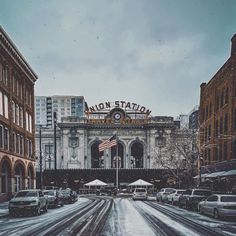 a snowy street with cars parked in front of an old station on the side of it