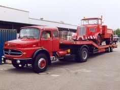 an old red tow truck parked in front of a building with other trucks behind it