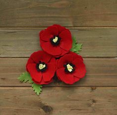 three red felt flowers with green leaves on top of wooden planks and one has a white heart in the center