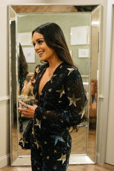 a woman standing in front of a mirror wearing a black dress with stars on it