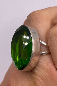 a close up of a person's hand holding a ring with a green stone