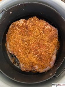 a large piece of meat in a slow cooker with seasoning sprinkled on top