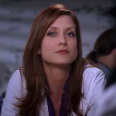 a woman with long brown hair and blue eyes looks at something in the distance while sitting down