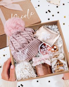 someone is holding a box filled with christmas items and gifts for the holiday season, including a pink beanie