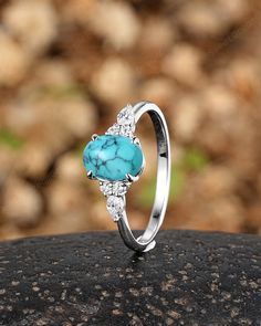 a turquoise stone and diamond ring sitting on top of a black rock in front of some rocks