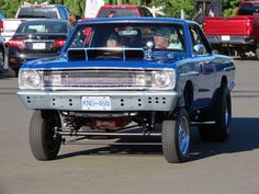 a blue truck driving down a street next to other cars and people in the back