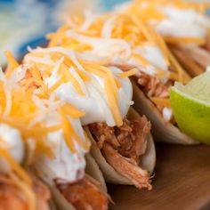 three tacos with shredded cheese, meat and a lime