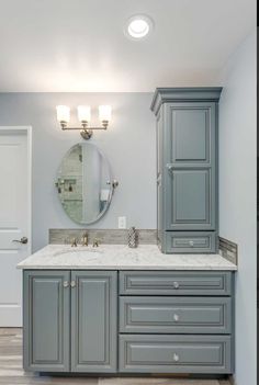 a large bathroom with gray cabinets and marble counter tops, along with a round mirror on the wall