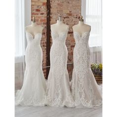 three wedding dresses on mannequins in front of a brick wall and window