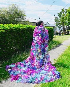 a woman is walking down the sidewalk in a colorful dress with feathers on it's back