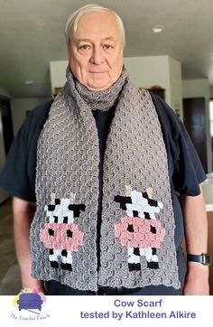 an older man wearing a gray scarf with pink and black cows on it, standing in front of a living room