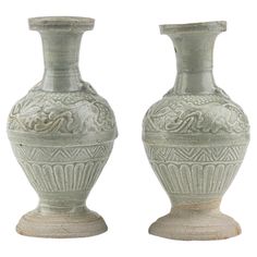 two white vases sitting side by side on top of each other, one with an intricate design