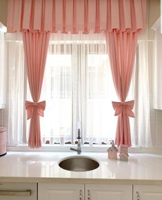 a kitchen sink under a window covered in pink curtained drapes and bowknots