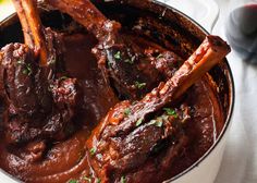 a pot filled with meat and sauce on top of a table next to a glass of wine