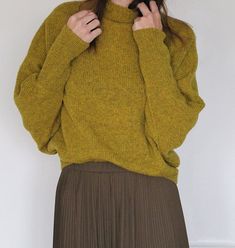 a woman wearing a green sweater and brown pleated skirt with her hands on her hips