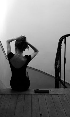 a woman sitting on top of a wooden floor next to a stair case in black and white