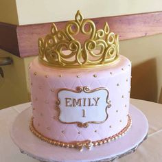 a pink and gold cake with a tiara on top is sitting on a table