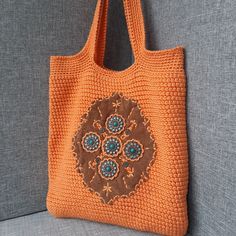 an orange crocheted bag hanging on the back of a gray couch with blue and brown beads