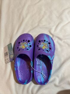 a pair of purple shoes sitting on top of a white bed next to a tag