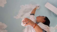 a woman is painting the ceiling with white paint and she has her hands in the air