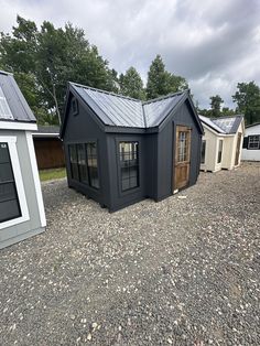 three tiny houses with metal roofs and windows on gravel ground in front of wooded area