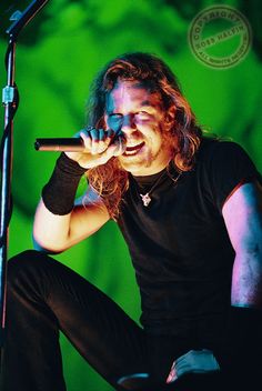 a man with long hair sitting on top of a stool while holding a microphone in his hand