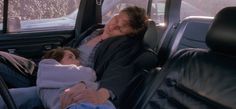 two people sleeping in the back seat of a car, one is holding a baby