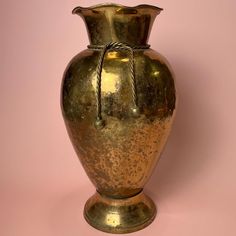 a gold colored vase sitting on top of a pink wall with a rope around it