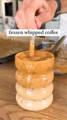 a person dipping something into a cup on top of a wooden table with the words frozen whipped coffee over it