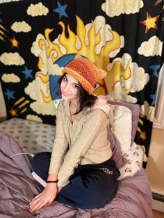 a young woman sitting on top of a bed wearing a knitted hat and sweater