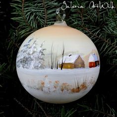 a glass ornament hanging from a tree with snow on the ground and houses painted on it