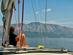 a woman sitting on the bow of a sailboat looking out at mountains in the distance