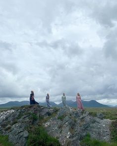 four women standing on top of a large rock in the middle of an open field