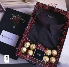 a black shirt and some chocolates in a box with red flowers on the table