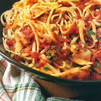 pasta with meat and tomato sauce in a black bowl on a wooden tablecloth next to a green towel