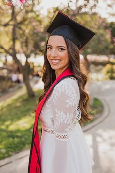 a woman wearing a graduation cap and gown posing for a photo in front of some trees