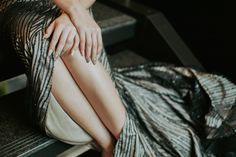 a woman sitting on top of a metal bench next to her hand resting on her leg