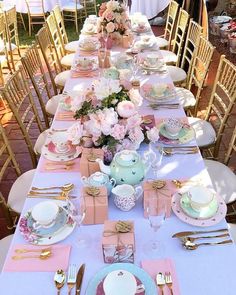 a long table with pink and white plates, silverware and flowers on it is set for a tea party