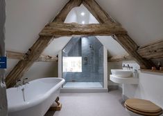 an attic bathroom with wooden beams and a white bathtub