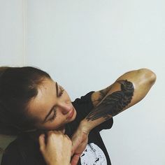 a woman with tattoos on her arm holding a bird in her right hand and looking at the camera